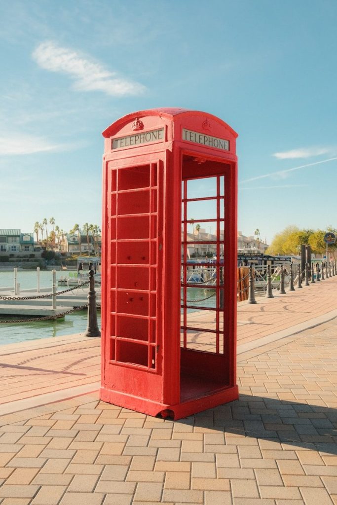 A red telephone booth stands by a waterfront.